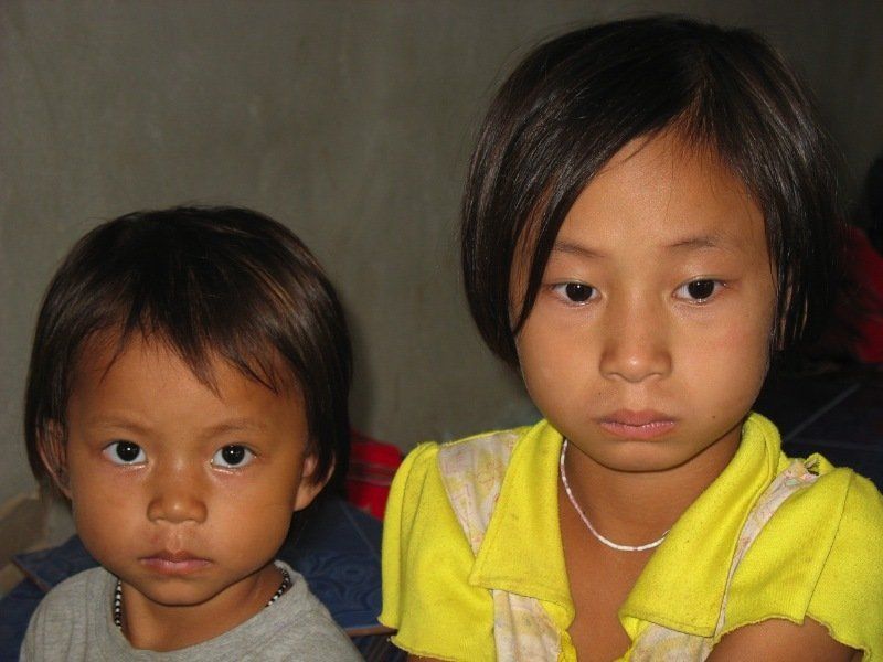 Two little girls are looking at the camera and one is wearing a yellow shirt