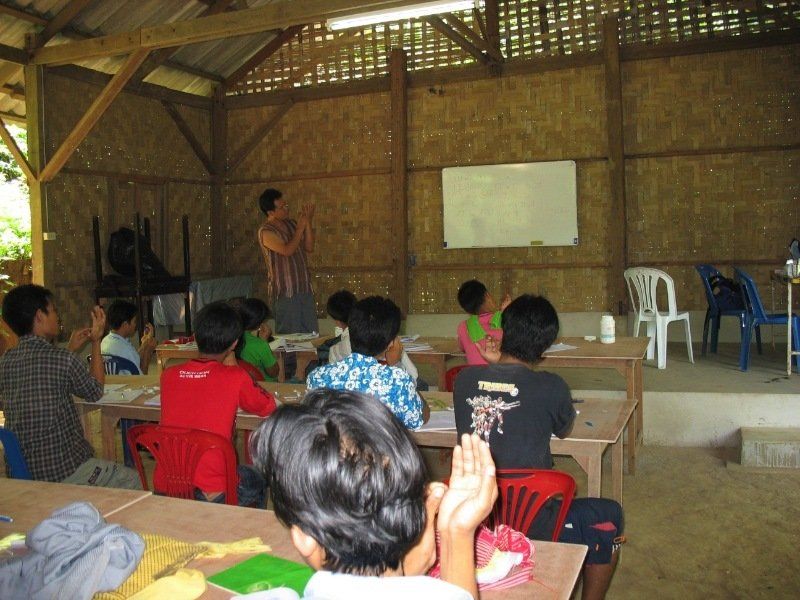 A group of children are sitting in a classroom with their hands up