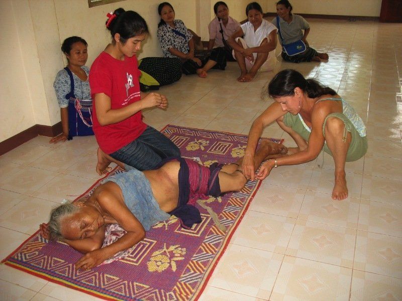 A woman in a red shirt is kneeling next to a man laying on a mat