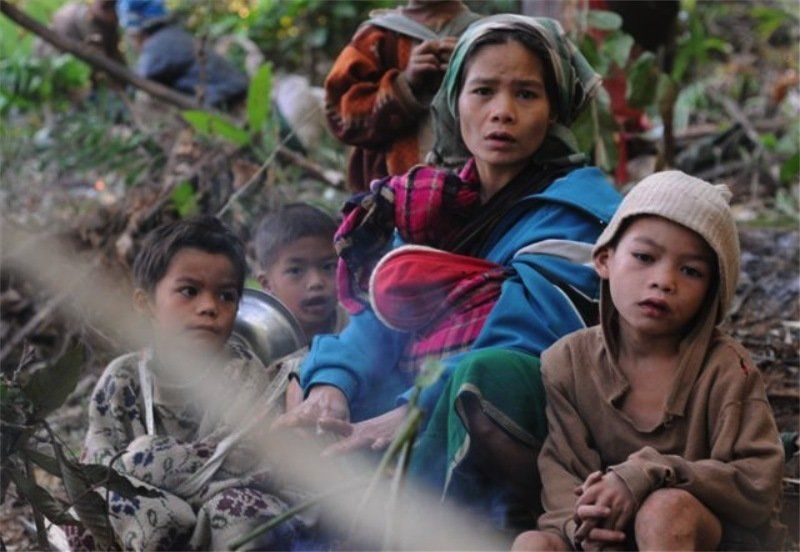 A group of children are sitting on the ground in the woods.