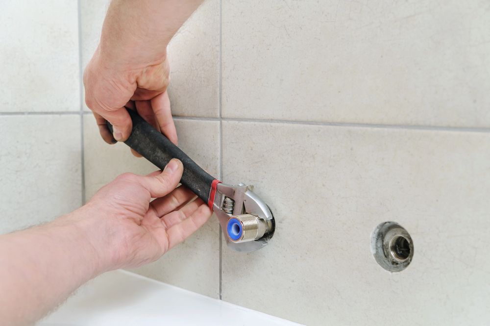 Hands using an adjustable wrench to tighten a metal plumbing fitting into a tiled wall.