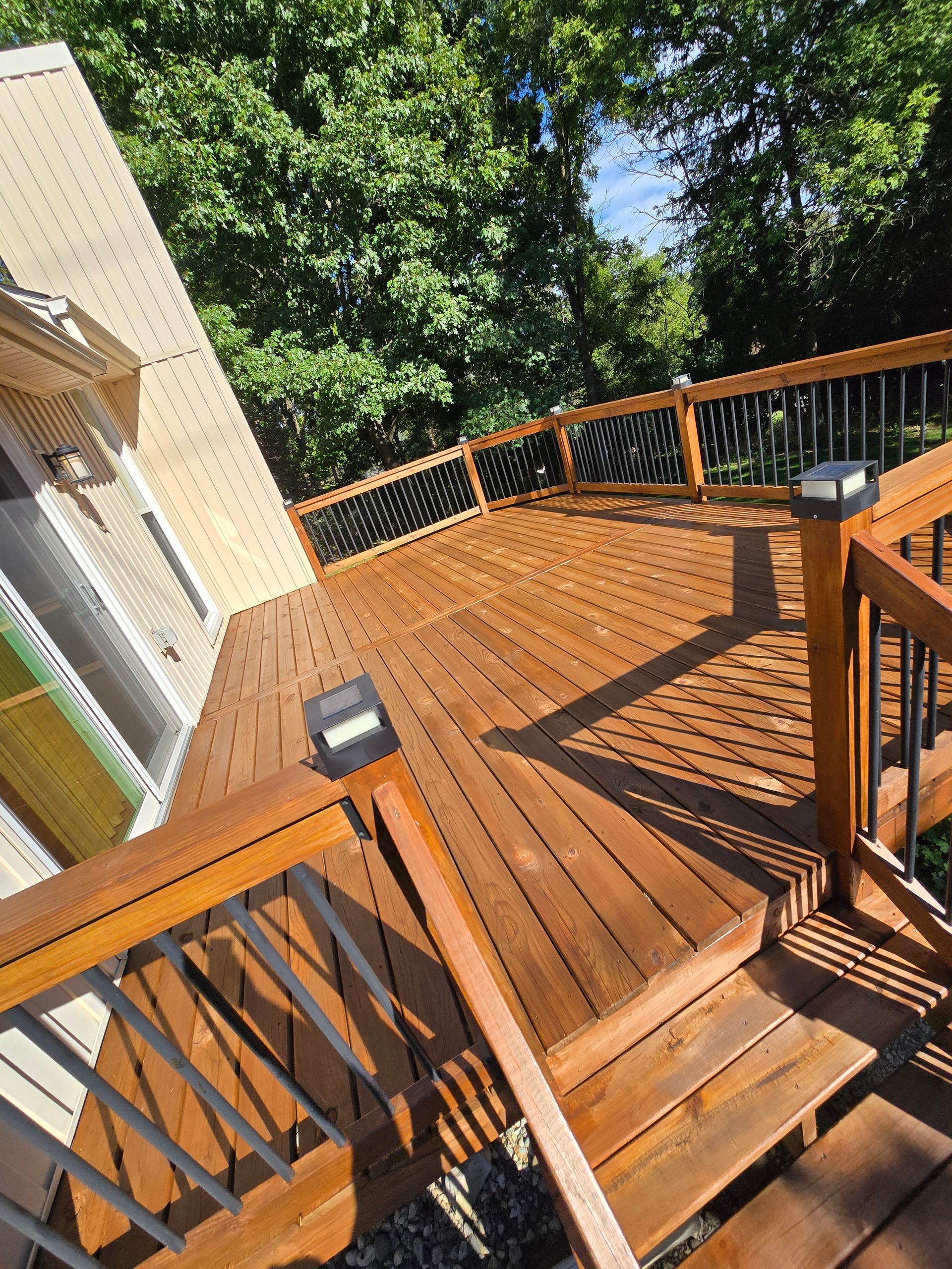 A wooden deck with stairs leading up to it and trees in the background.