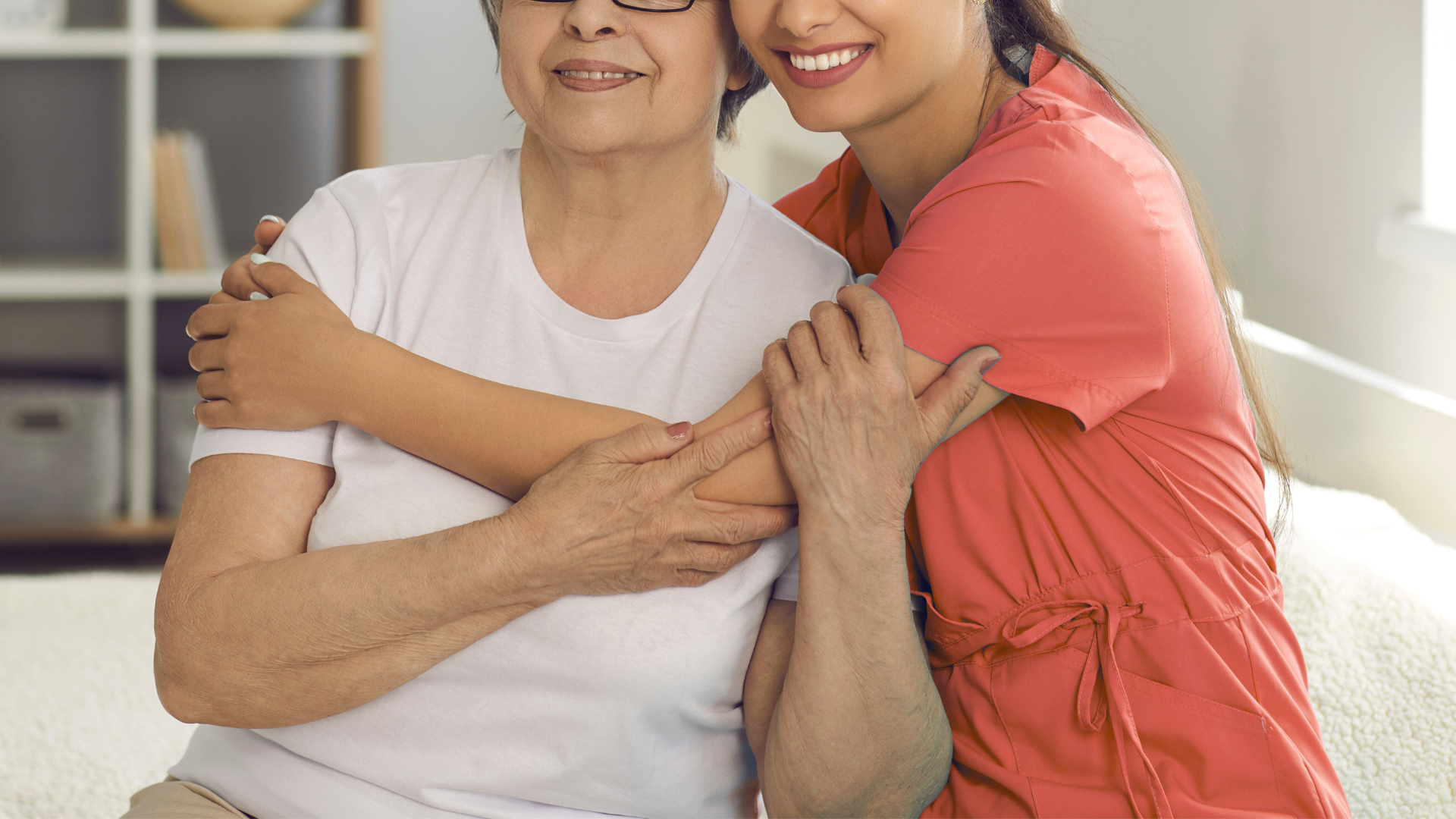 Young woman hugs older woman indoors; both smile.