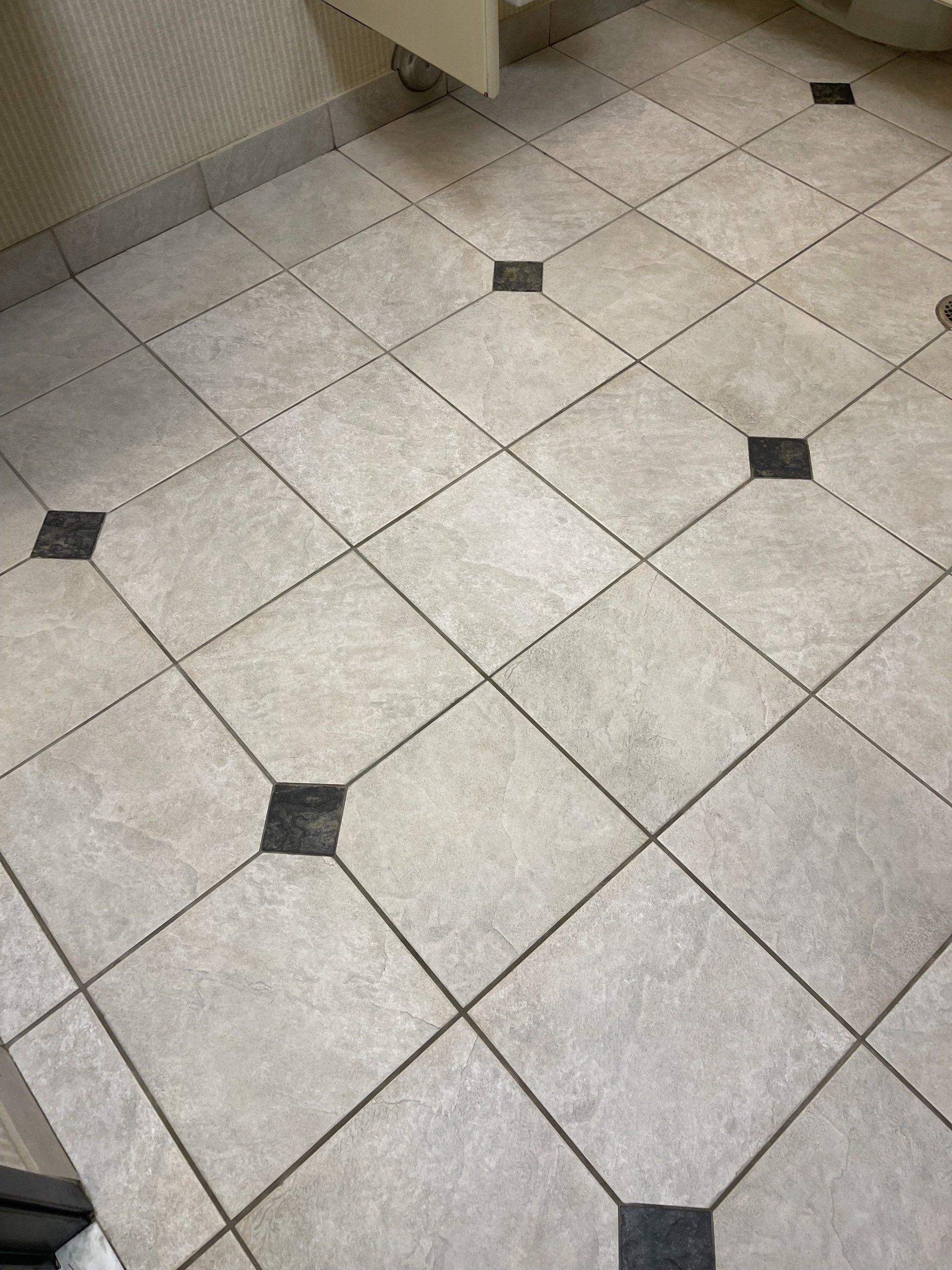 A bathroom floor with white tiles and black squares.