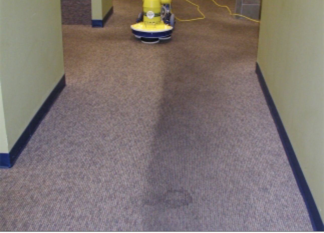 A yellow vacuum cleaner is cleaning a carpet in a hallway