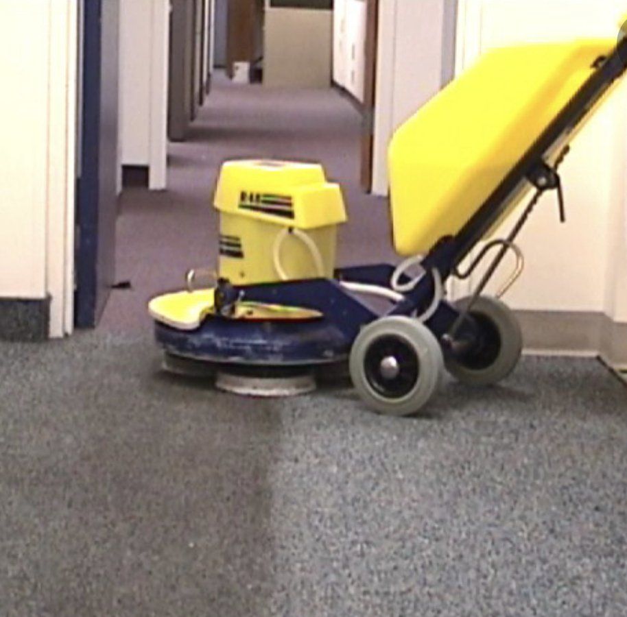 A yellow and blue machine is cleaning a carpet in a hallway