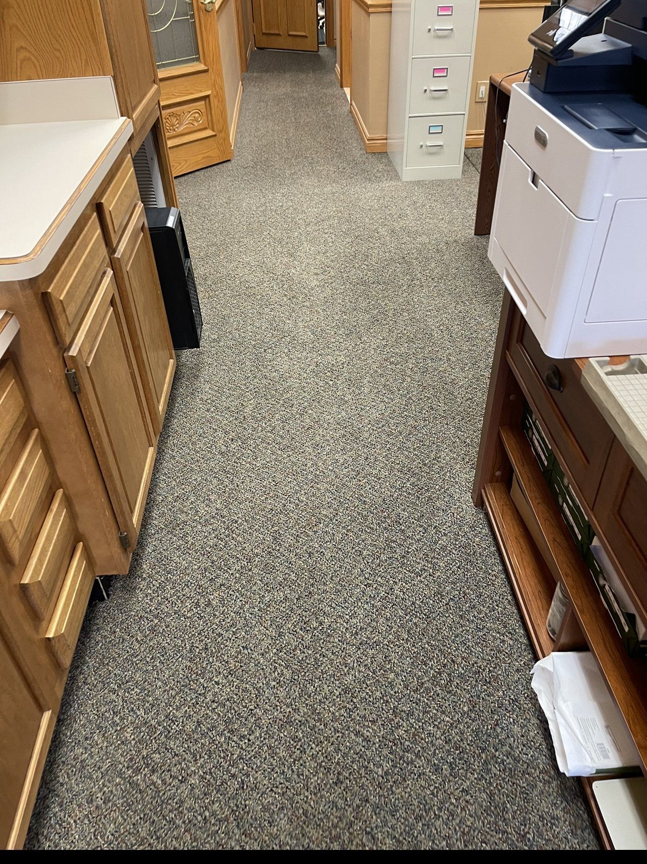 A long hallway with a printer and cabinets in a kitchen.