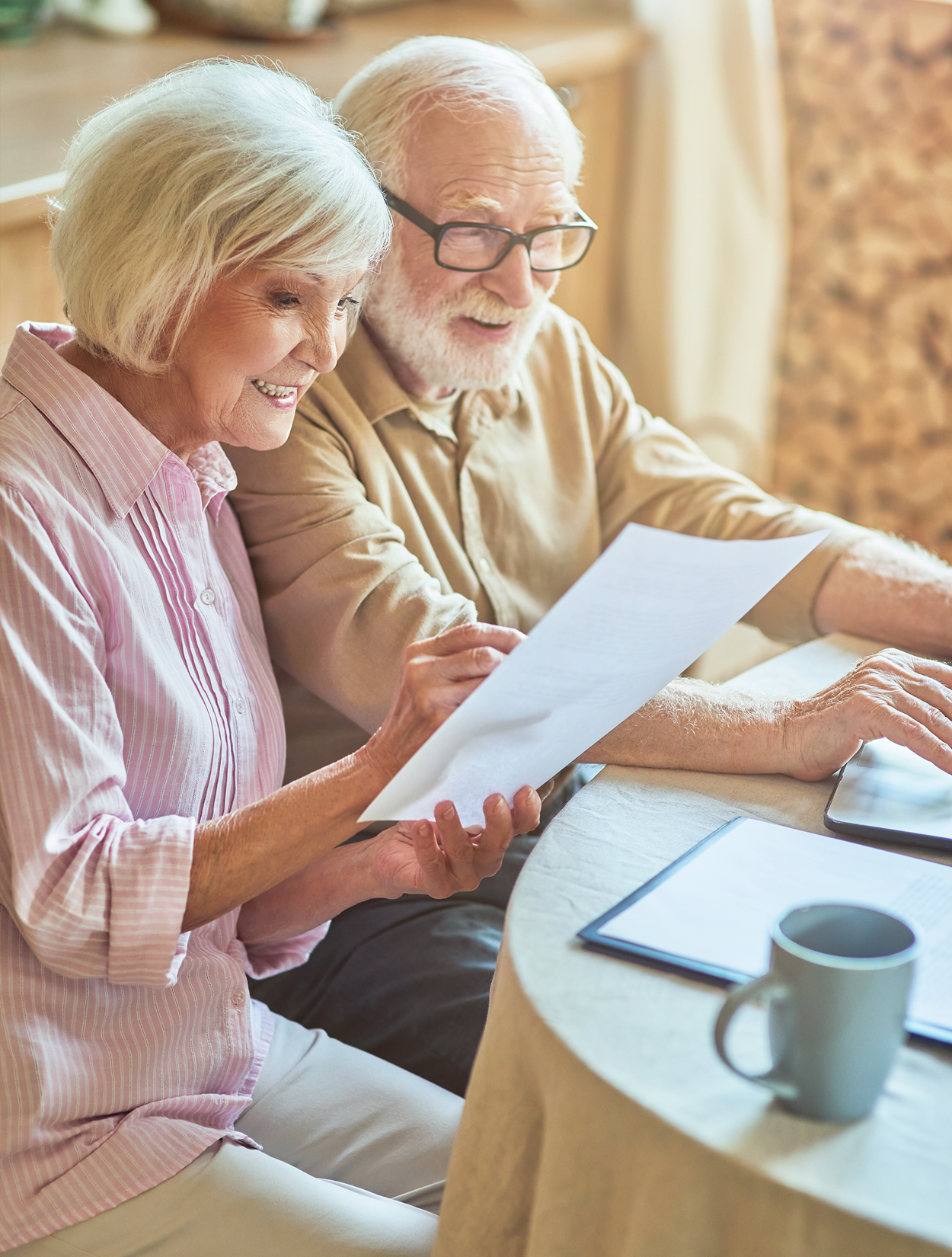 An elderly couple is sitting at a table looking at a piece of paper.