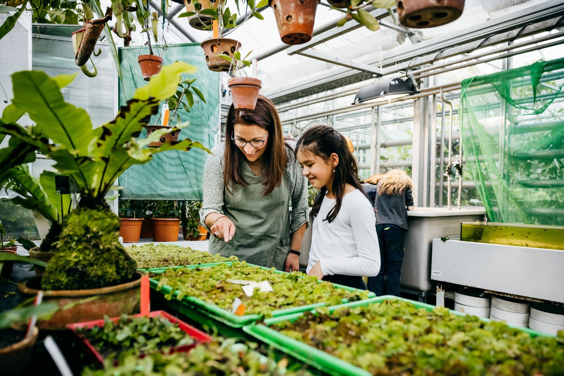 A woman showing a young girl some seedlings in a nursery.