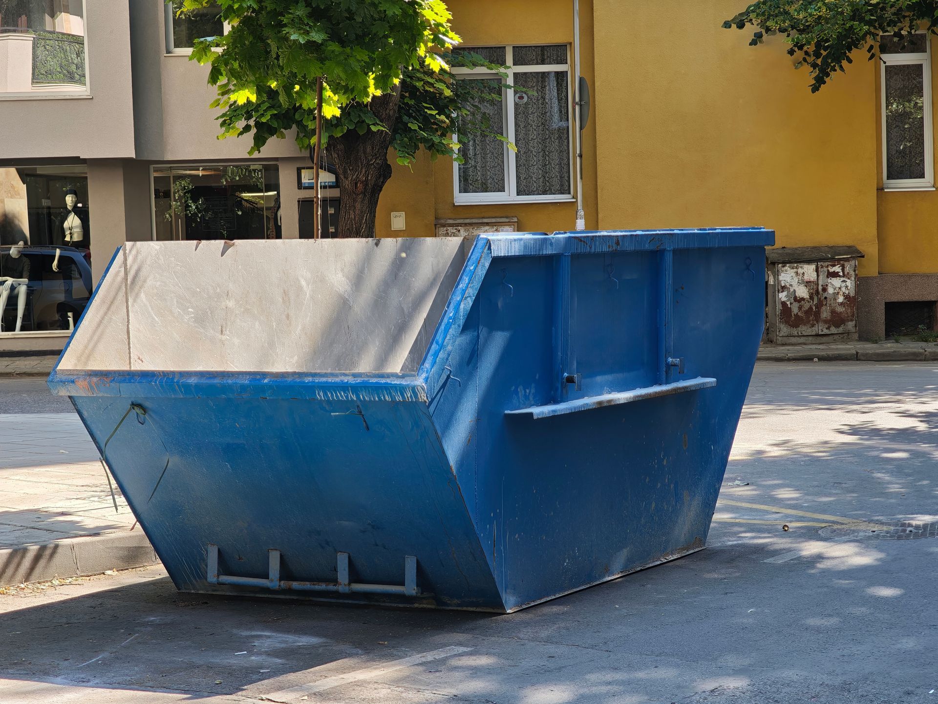 Large blue commercial dumpster placed on a city street for waste disposal. Large blue commercial dumpster placed on a city street for waste disposal.