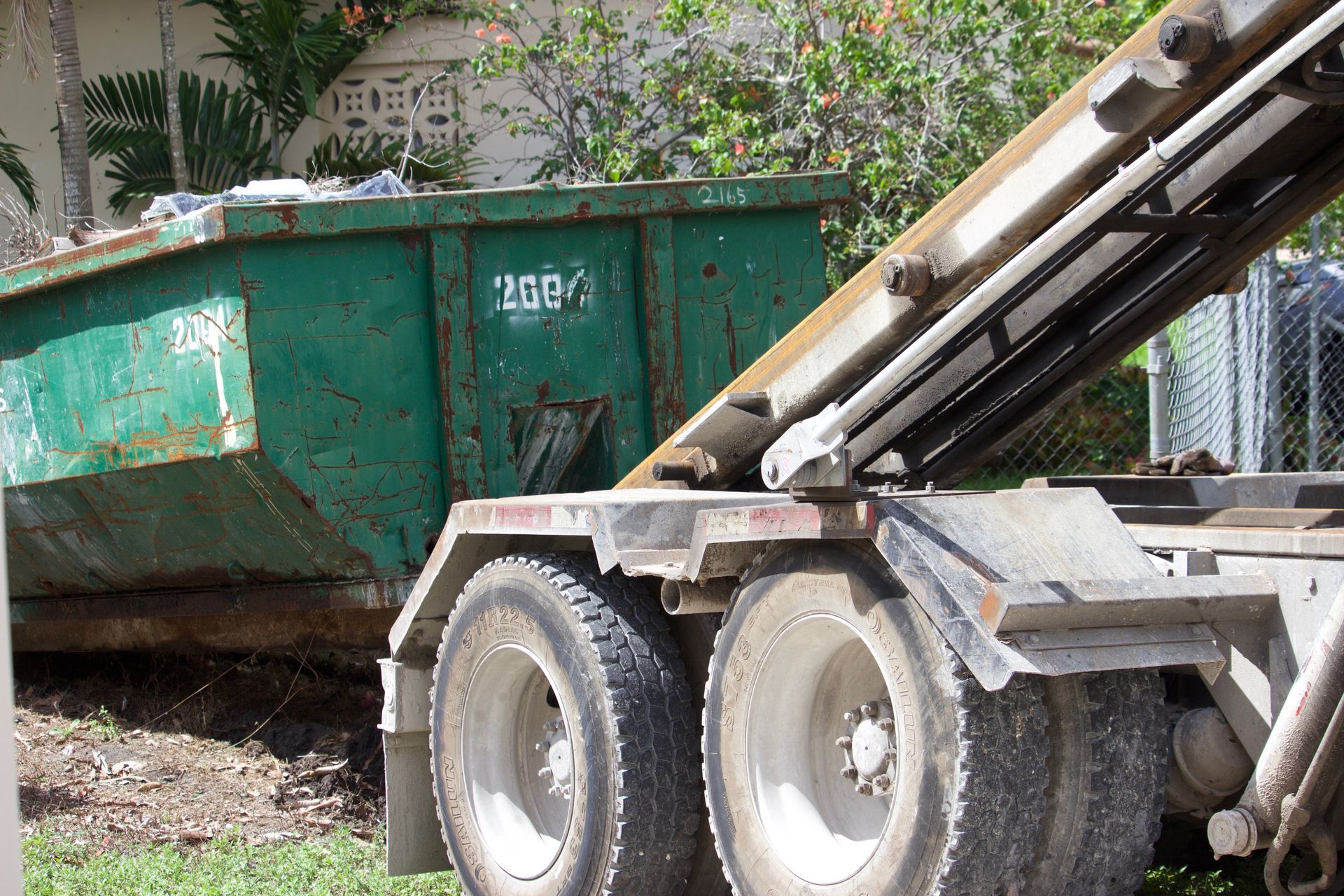 Green construction dumpster beside a truck loading debris in a residential yard. Green construction dumpster beside a truck loading debris in a residential yard.