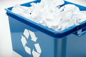 A blue recycling bin filled with crumpled paper.