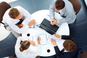 A group of people are sitting around a table with a laptop.