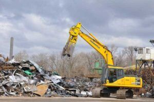 A yellow excavator is working on a pile of scrap metal.