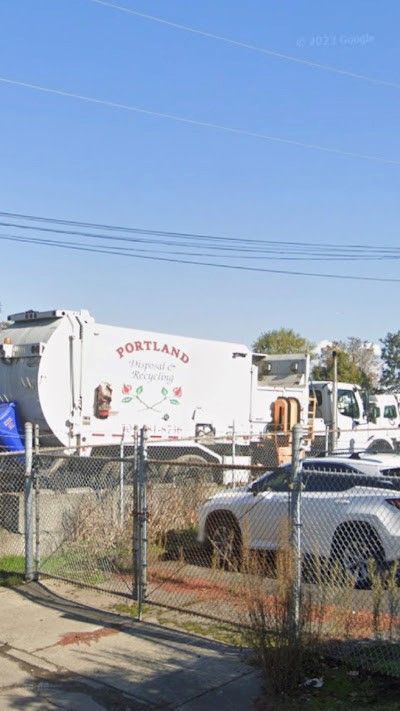 A garbage truck is parked in a parking lot next to a fence.