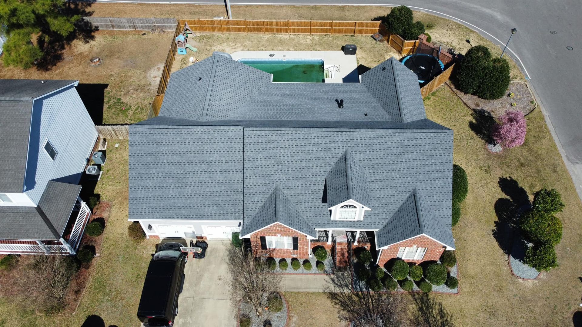 Aerial view of a two-story brick home with a pool in the backyard and a black vehicle in the driveway.