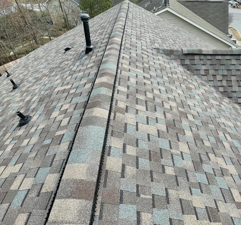 Close-up of a multi-colored shingle roof with a vent pipe and other roof features.
