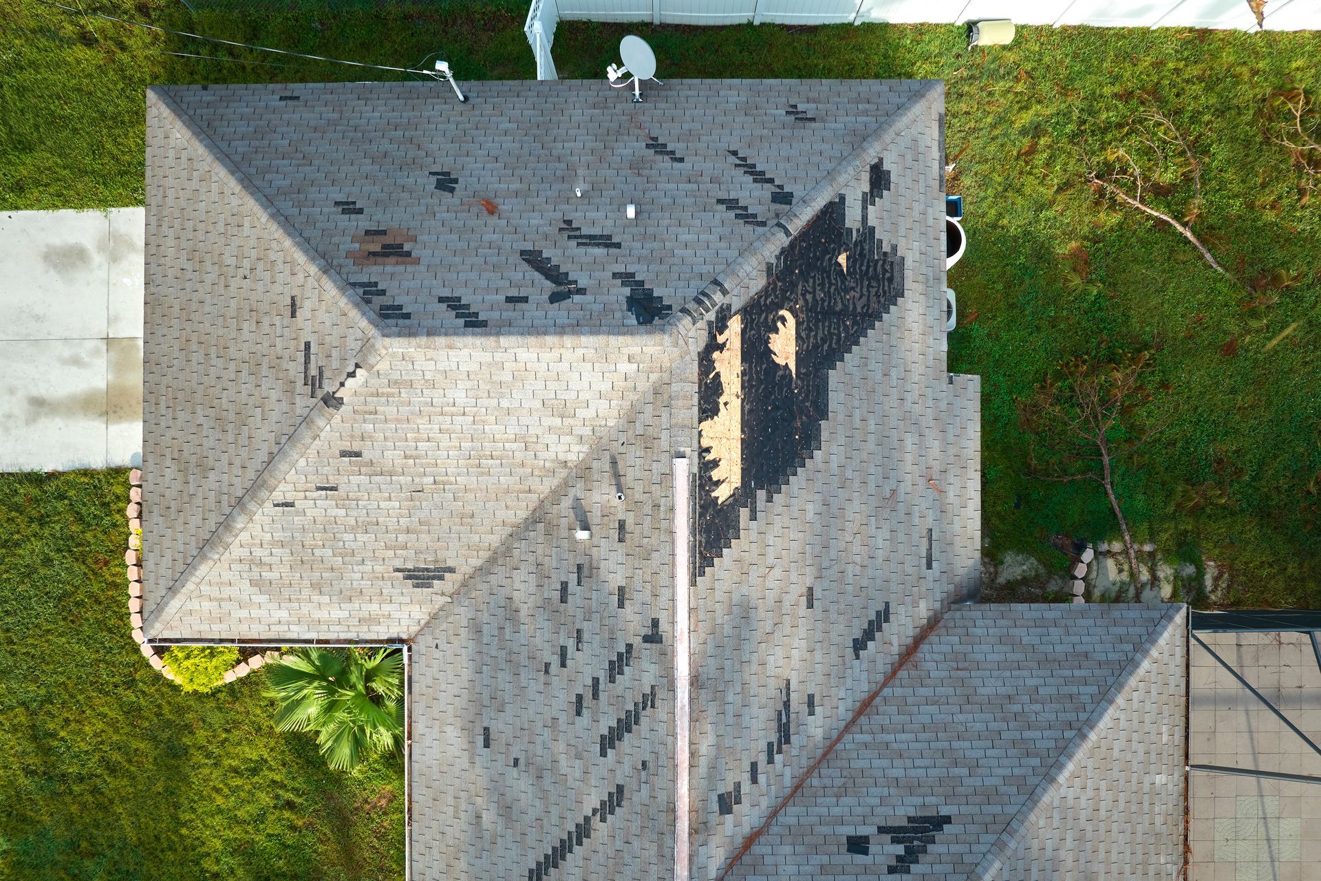 Overhead view of a gray roof with missing shingles; surrounded by green grass and a white walkway.