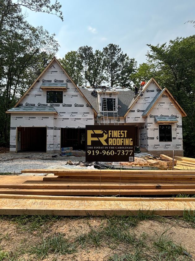A house under construction with a sign for finest roofing in front of it.