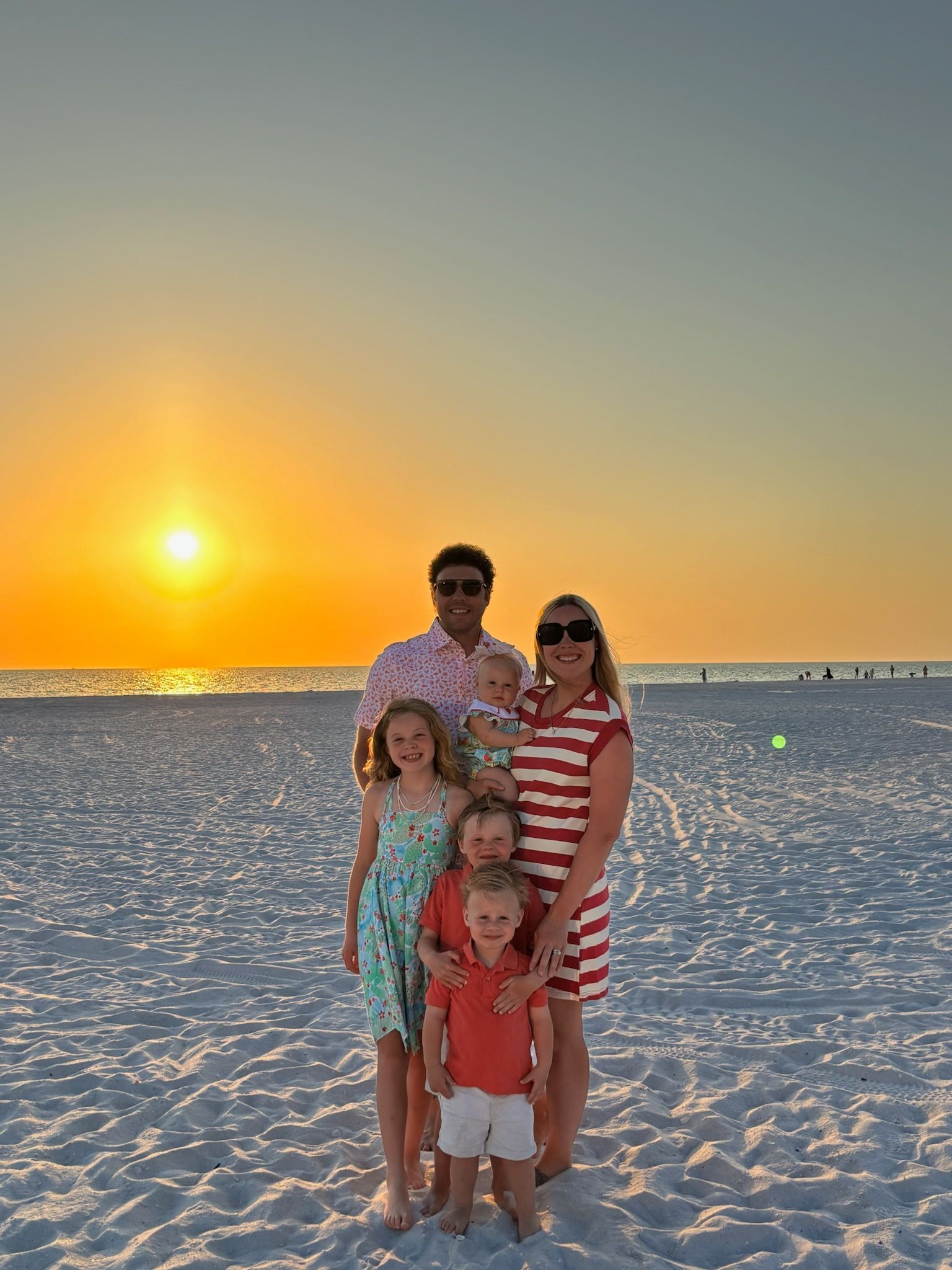 A family is posing for a picture on the beach at sunset.
