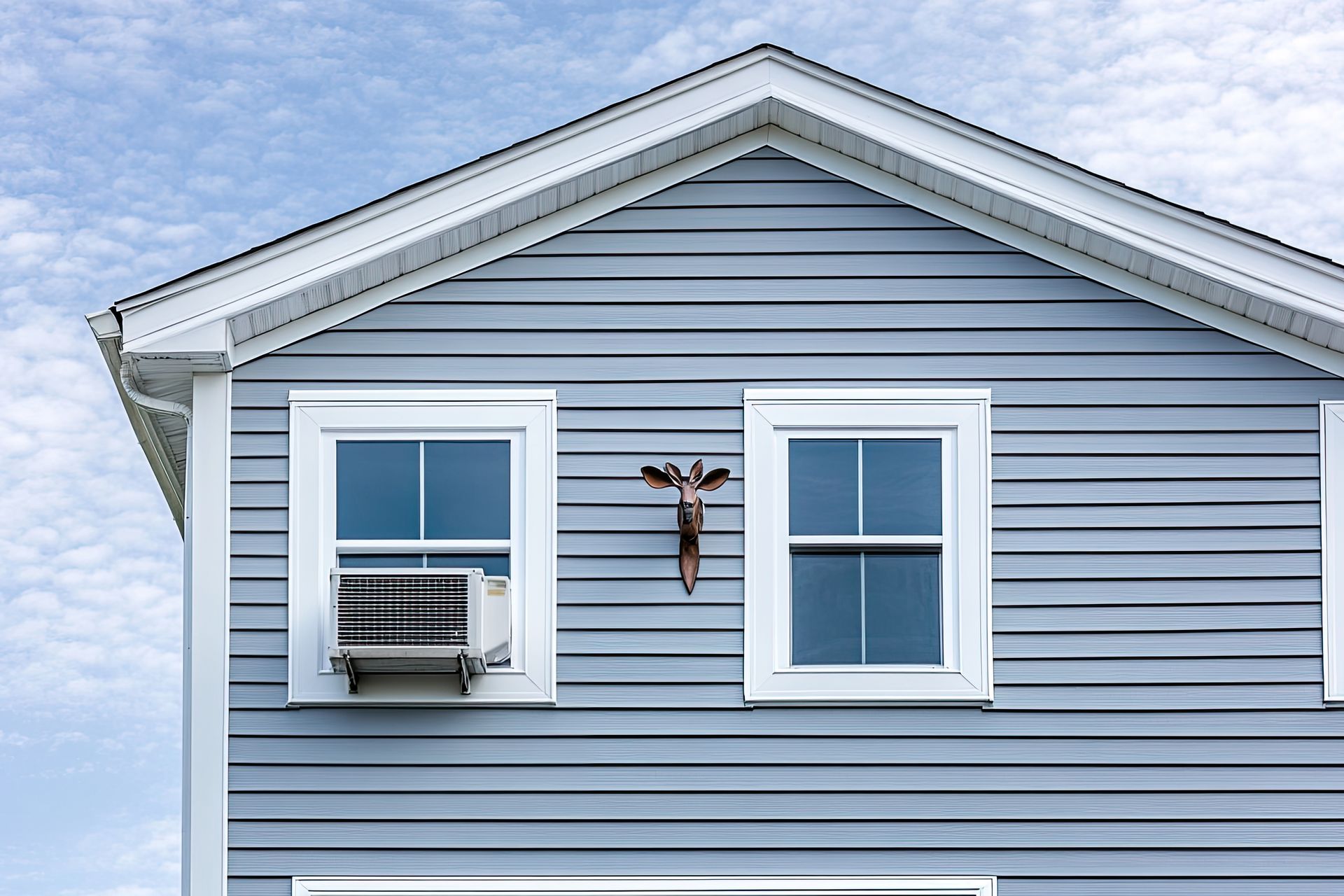 Blue house with white trim, two windows, an AC unit, and a giraffe head sculpture.