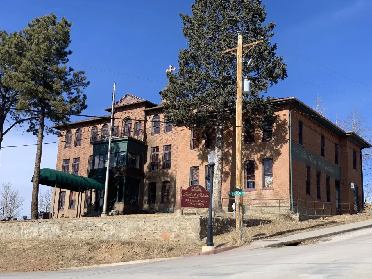 A large brick building is sitting on top of a hill with trees in front of it.