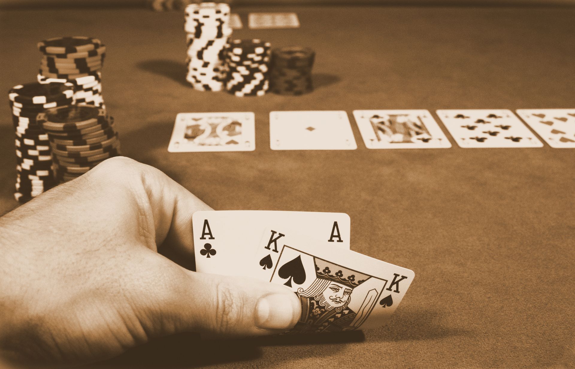 A hand holding two aces in front of a poker table