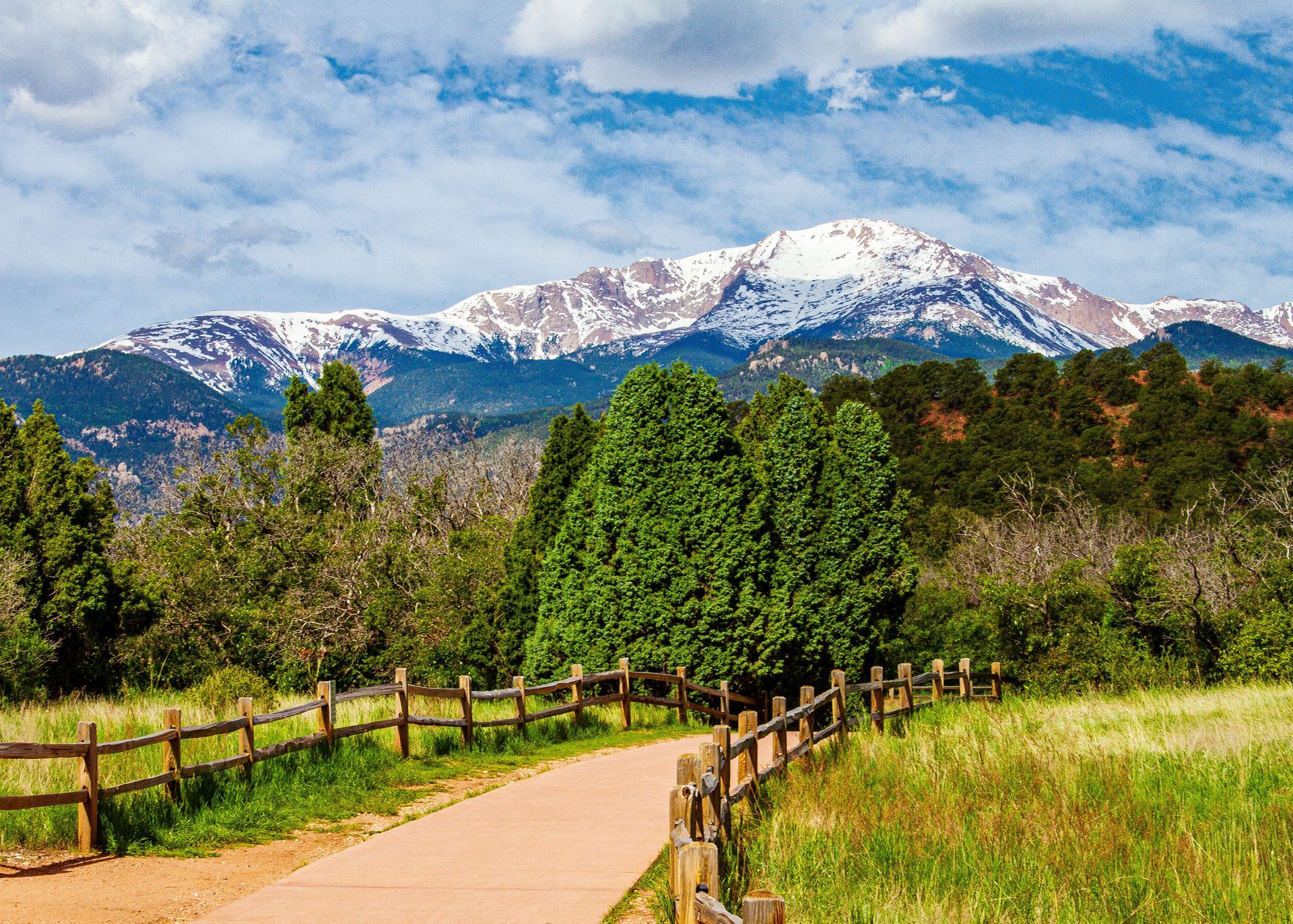A path going through a grassy field with a wooden fence and mountains in the background.