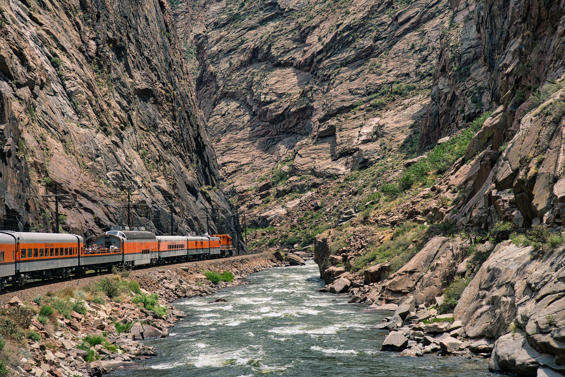 A train is going down a mountain next to a river.