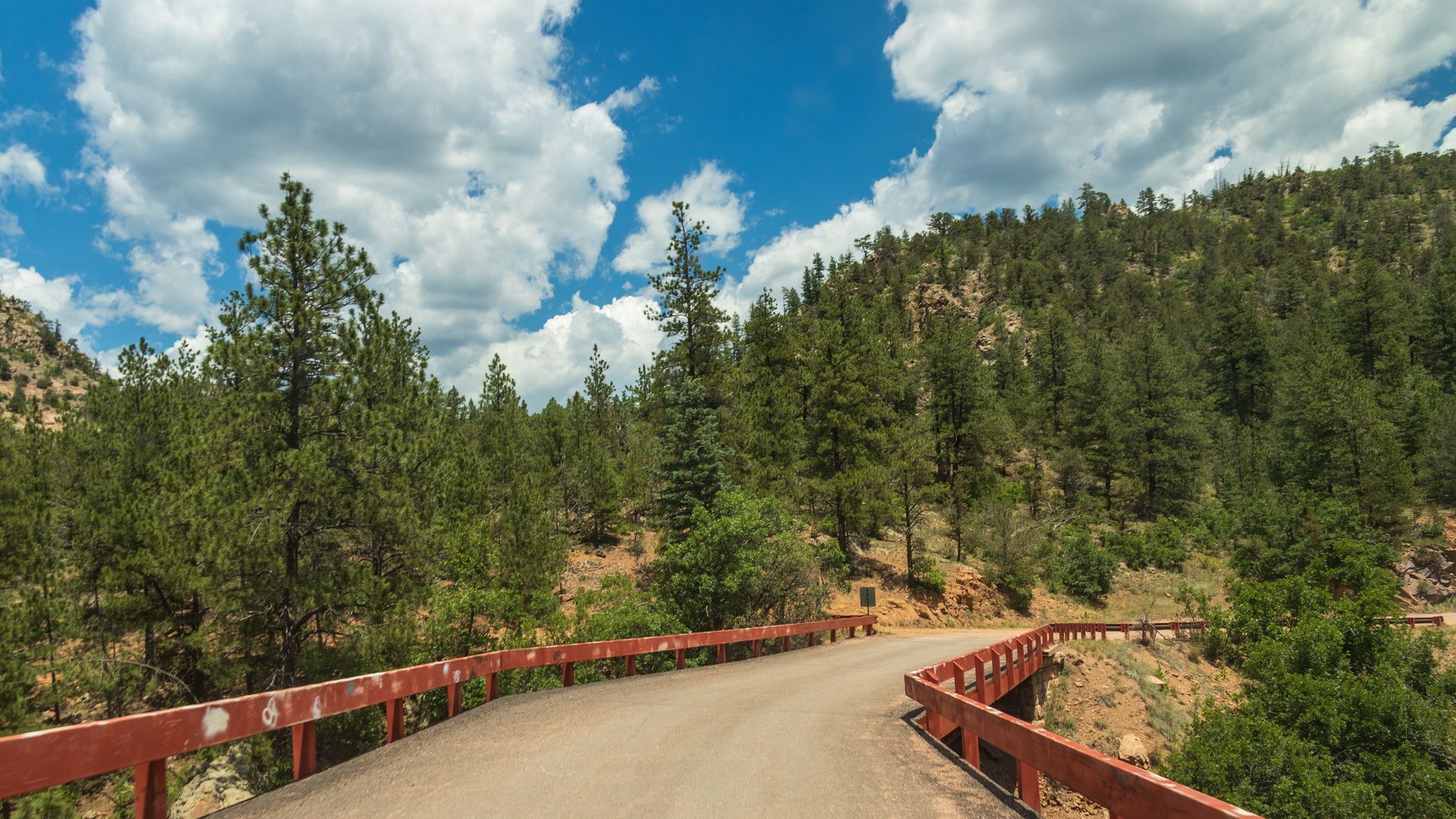 A bridge over a road in the mountains with trees on both sides.
