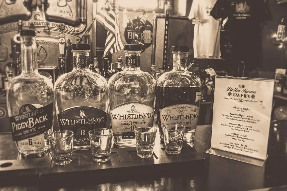 A black and white photo of bottles and shot glasses on a bar.