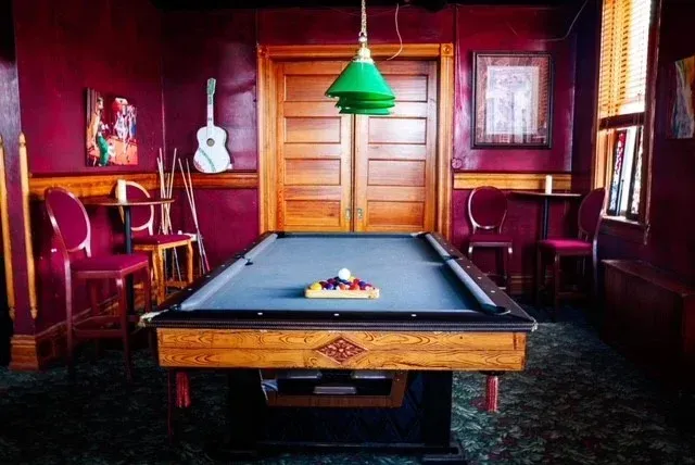 A pool table with a green light hanging from the ceiling