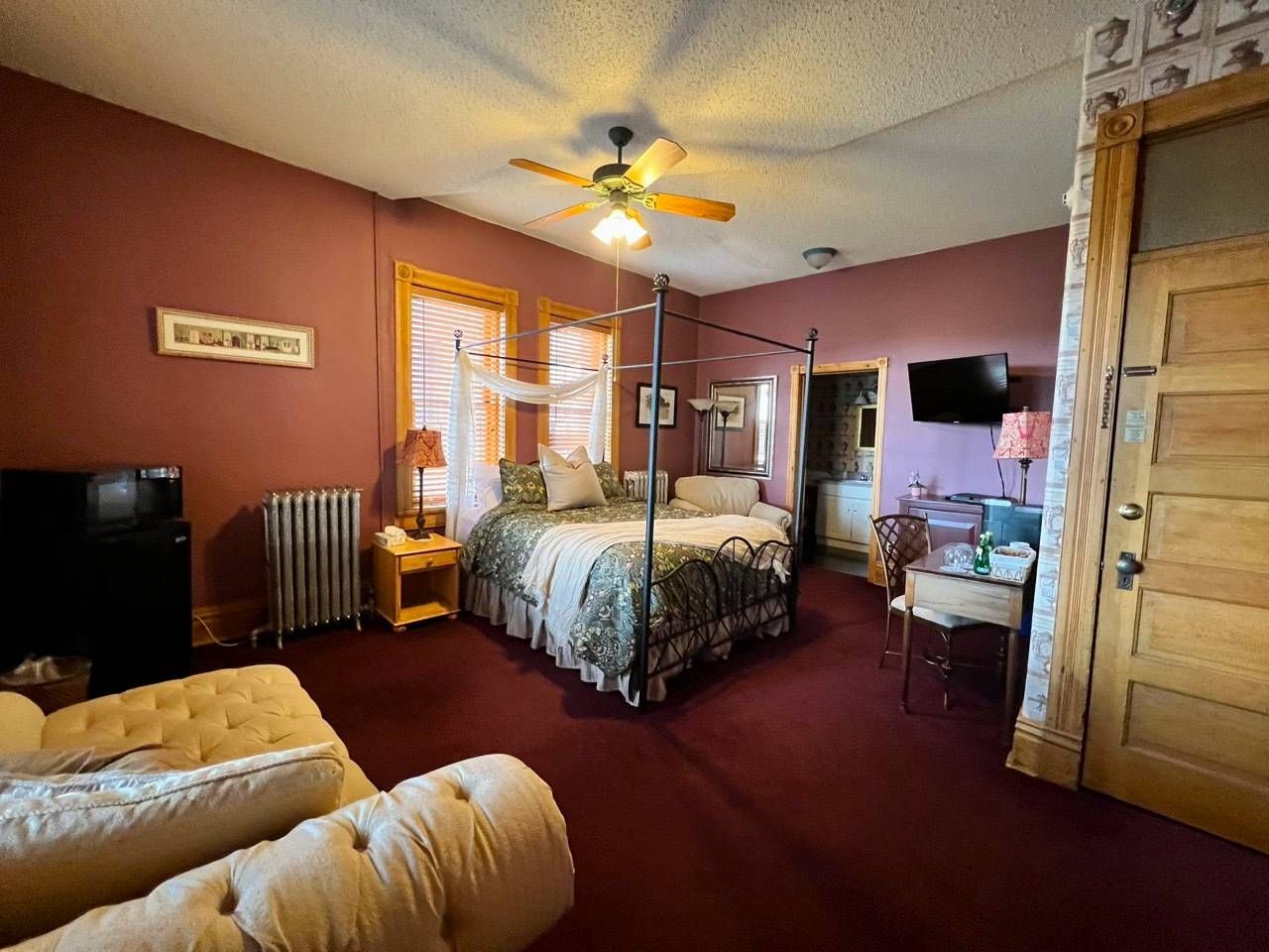 A bedroom with a four poster bed , a couch , a television and a fireplace.