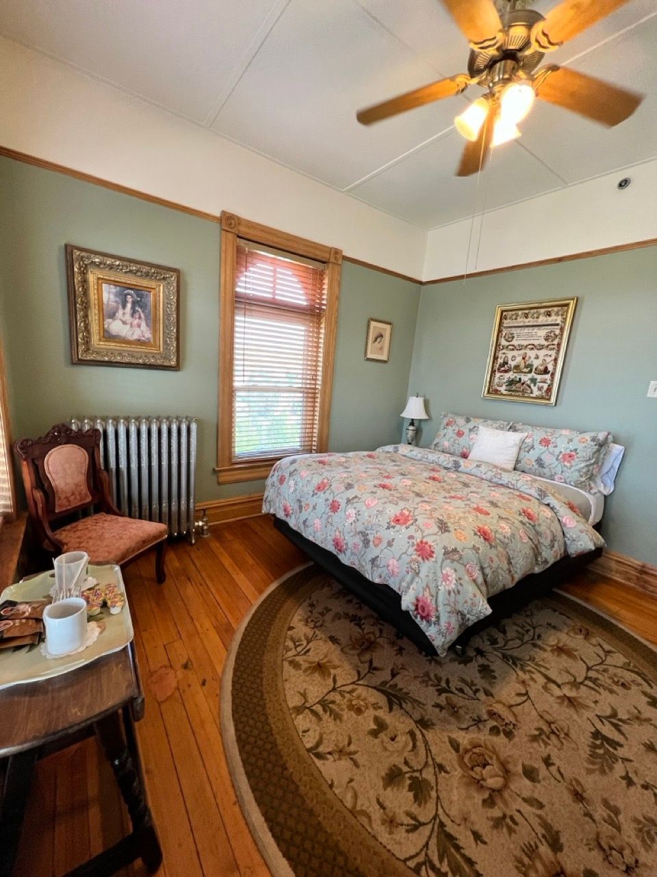 A bedroom with a bed , chair , table and ceiling fan.