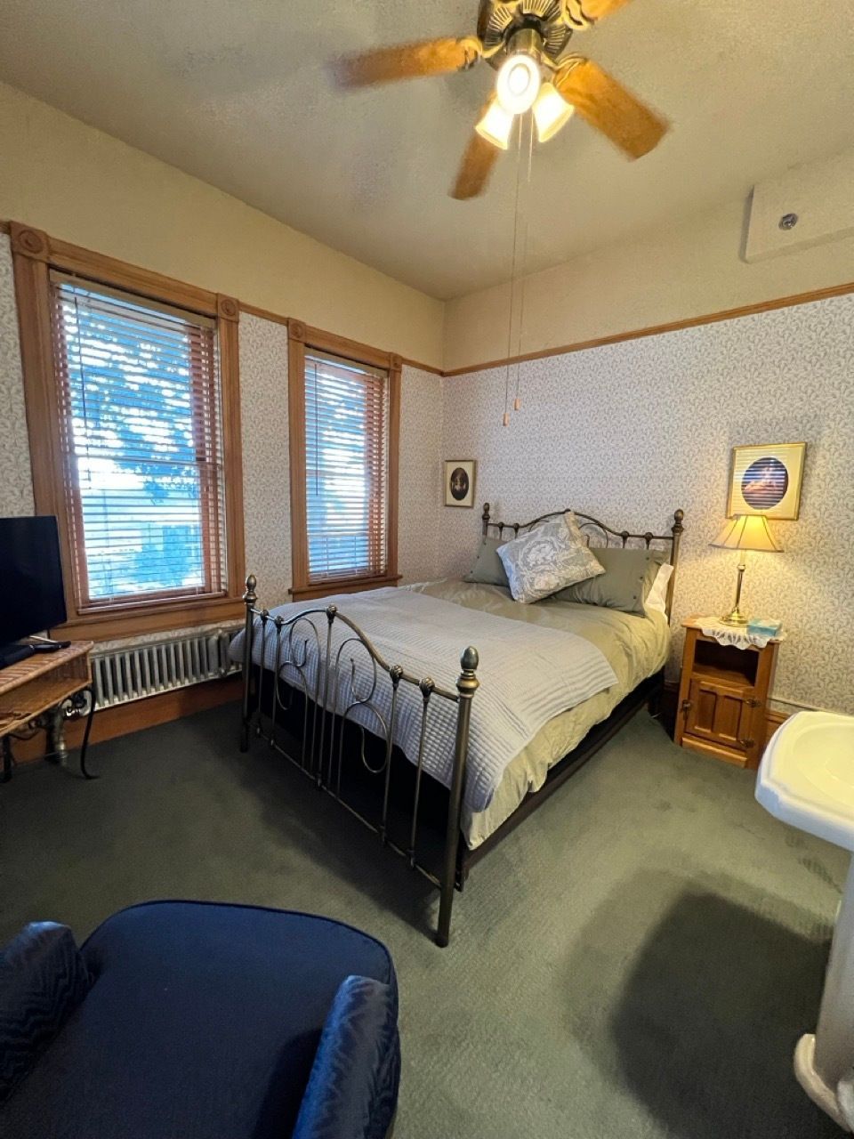 A bedroom with a bed , chair , television , sink and ceiling fan.