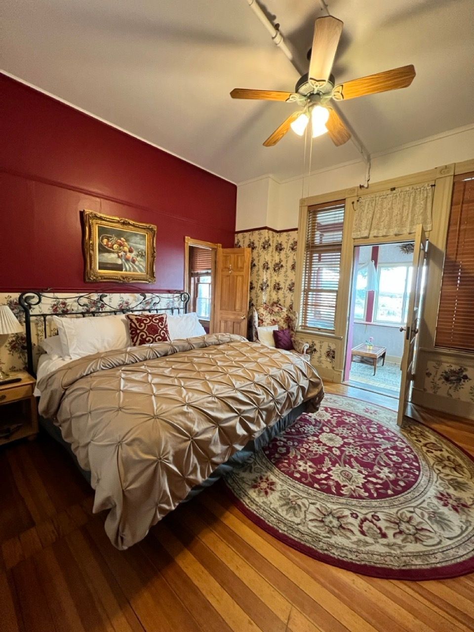 A bedroom with a bed , rug , ceiling fan and red walls.