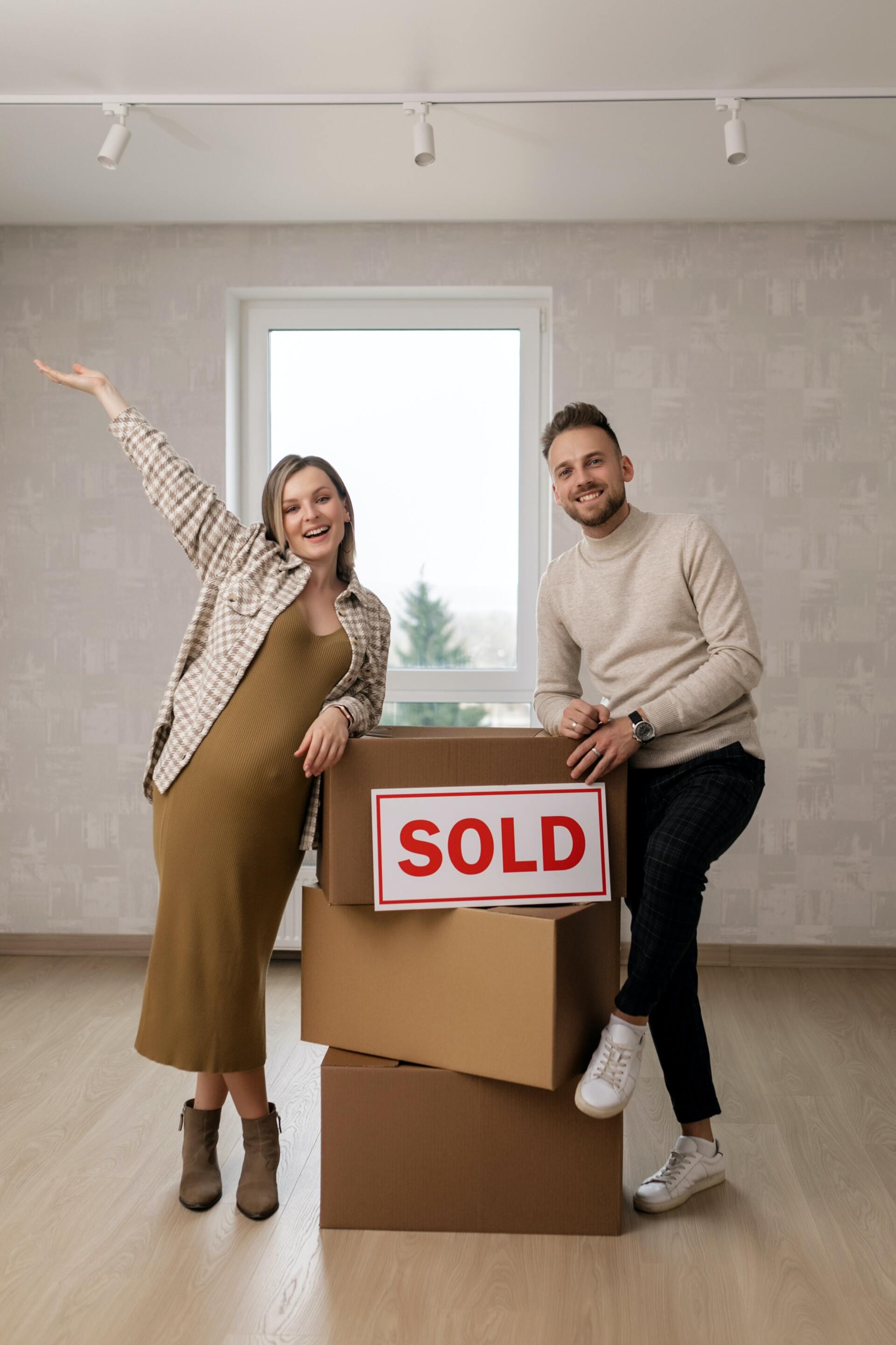 Couple next to moving boxes and sold sign