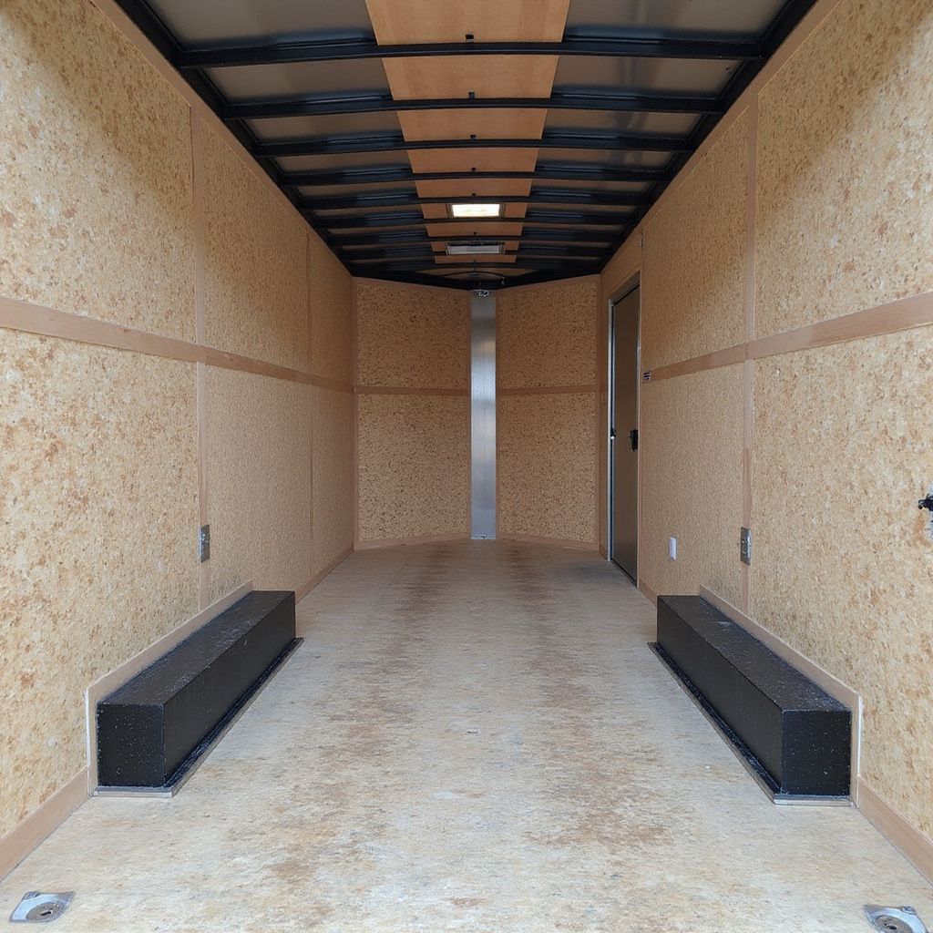 Interior view of an empty cargo trailer with light-colored particleboard walls, a gray floor, and black support beams.