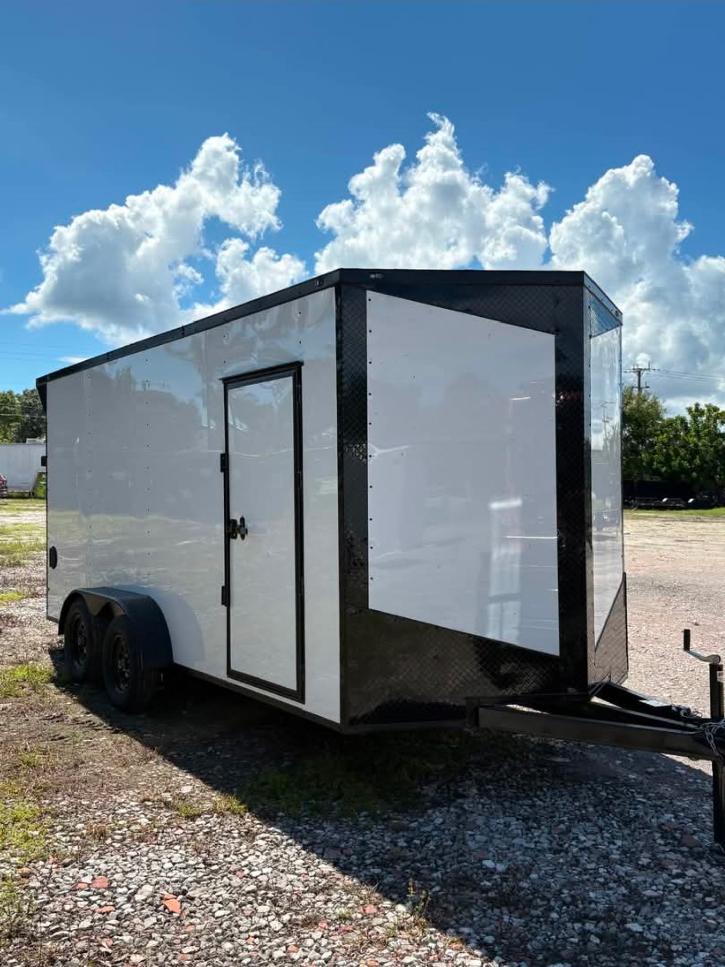 White enclosed trailer with black trim, parked outside under a cloudy sky.