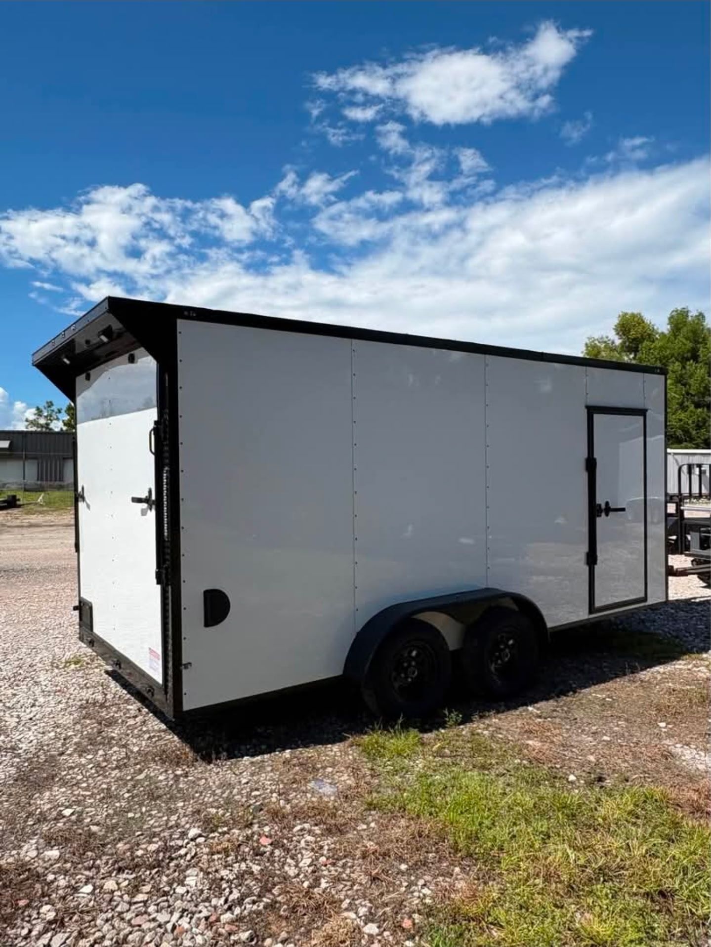 White enclosed trailer with black trim and wheels parked outside on grass.