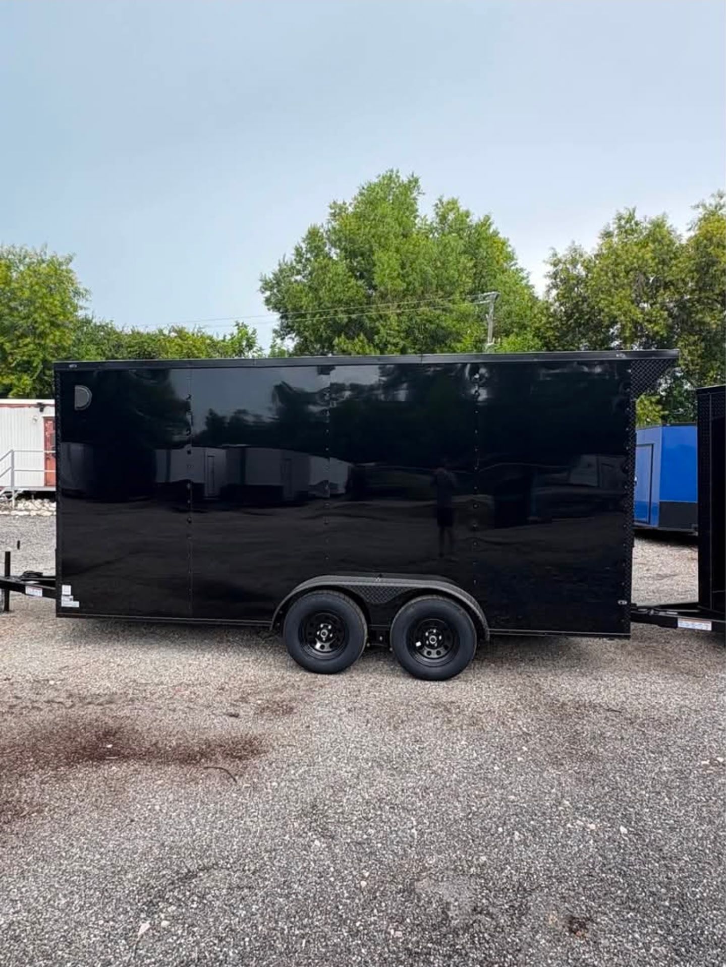 Black enclosed trailer with two wheels on gravel.