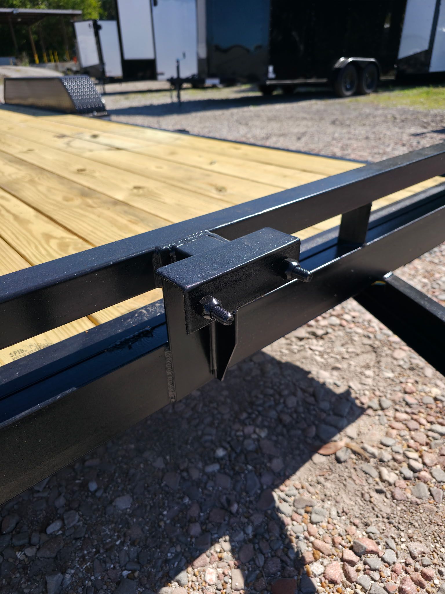 Black metal trailer frame with a bracket and wood decking in an outdoor setting.