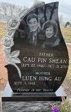Black granite teardrop-shaped tombstone with etched portraits of a couple and carved flowers.