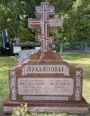 Red and gray Russian Orthodox grave marker with cross, text, and names in a cemetery.