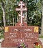 Red granite monument on a base featuring an Orthodox cross and engraved Cyrillic lettering.