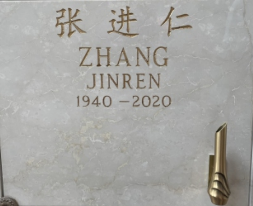 A light grey granite mausoleum door with Chinese characters and an English translation.