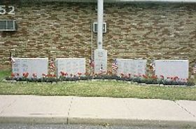 A civic memorial with five stone markers and a flagpole in front of a brick building