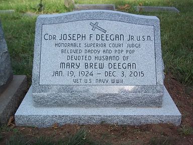 A single slant grey granite headstone with a polished surface, featuring military and religious symbolism