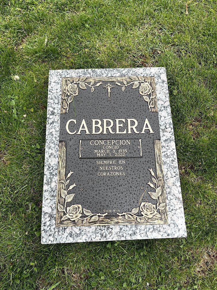 Black bronze grave marker with gold lettering and floral border on granite. In the grass.