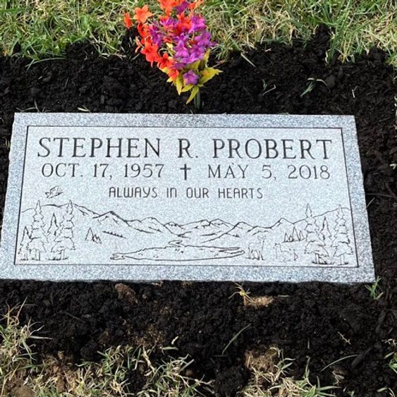 A flat granite footstone with an engraved mountain scene with trees and a lake.